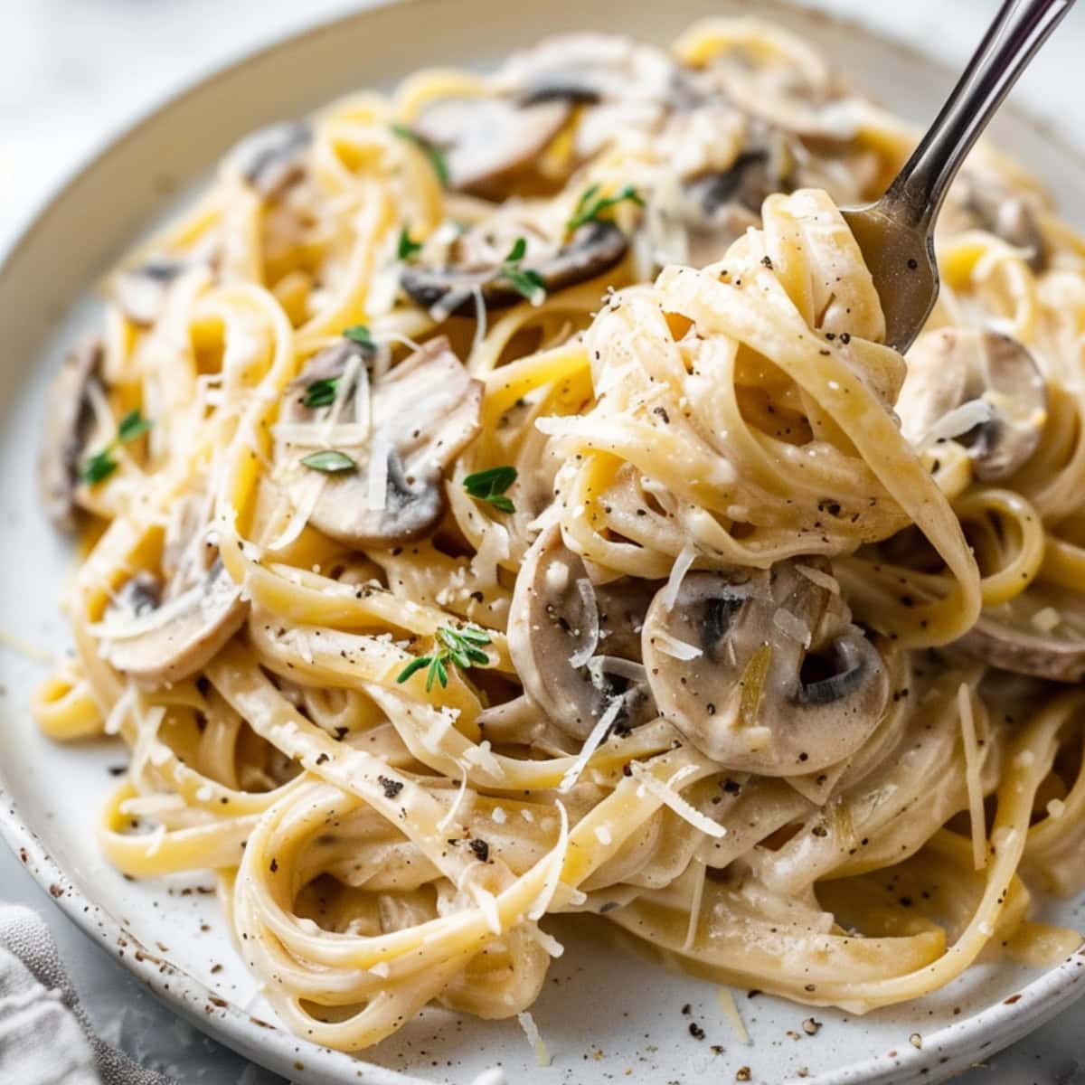 Fork lifting a serving of creamy mushroom pasta from plate.