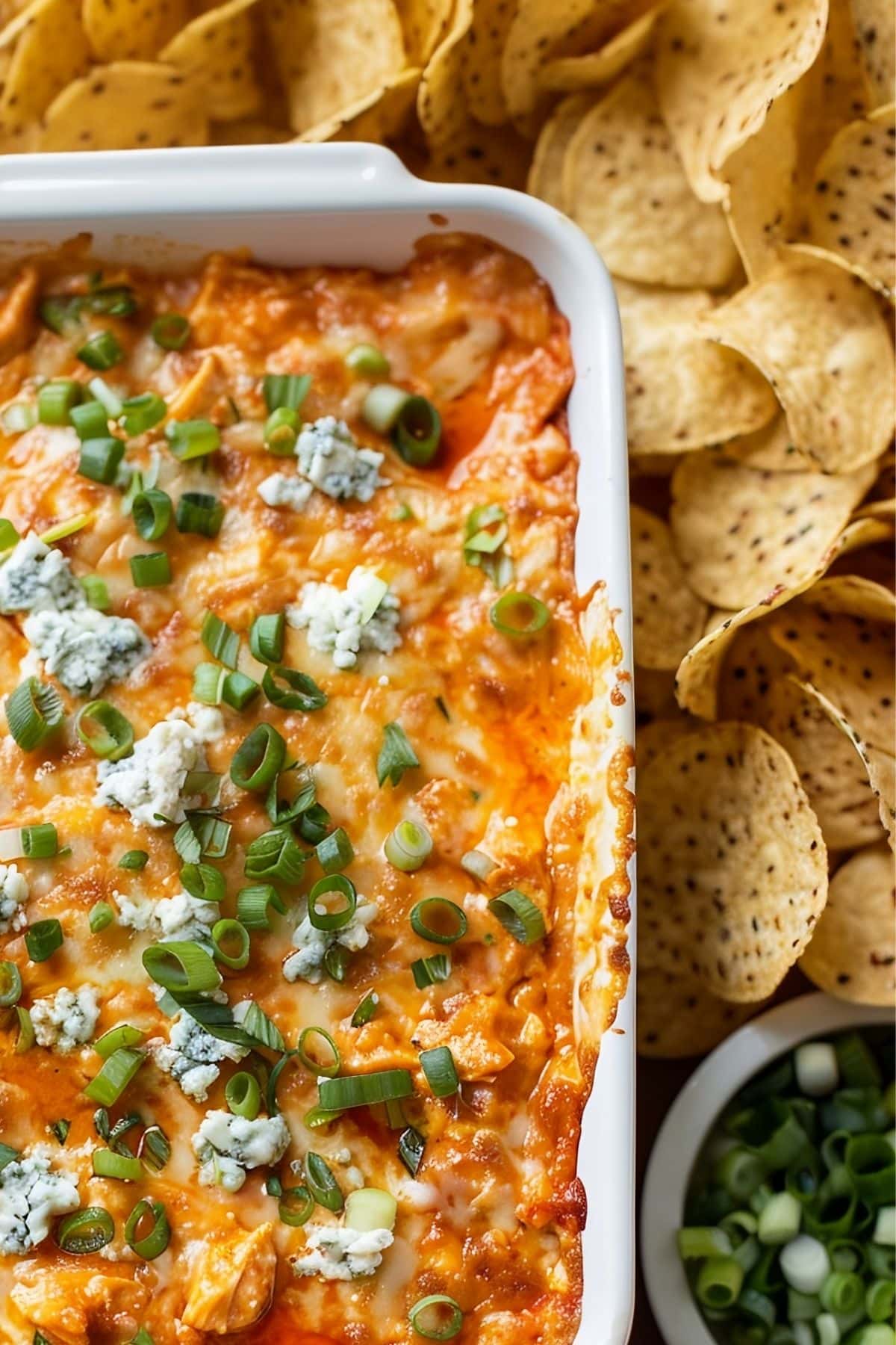Close Up Top View of Frank's Buffalo Chicken Dip in White Casserole Dish with a Bowl of Green Onions and Tortilla Chips