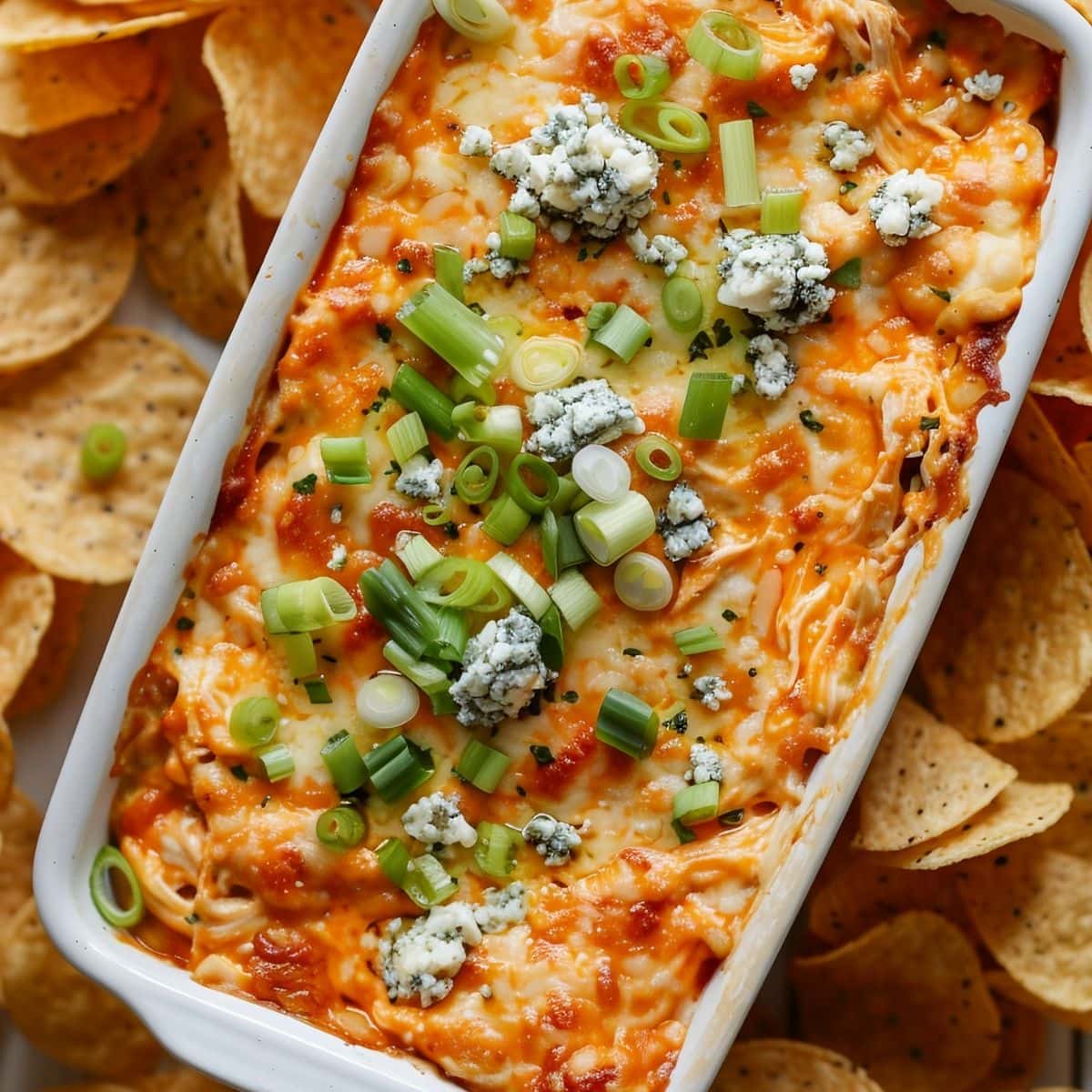 Top View of Frank's Buffalo Chicken Dip in a White Casserole Dish with Green Onions and Bleu cheese and Chips All Around the Dish