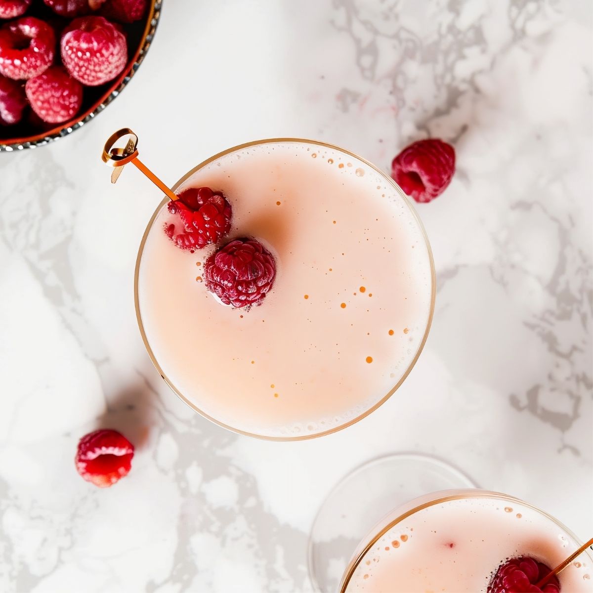 Top View of Two Foamy French Martinis with Raspberries for Garnish on a White Marble Table with a Bowl of Raspberries