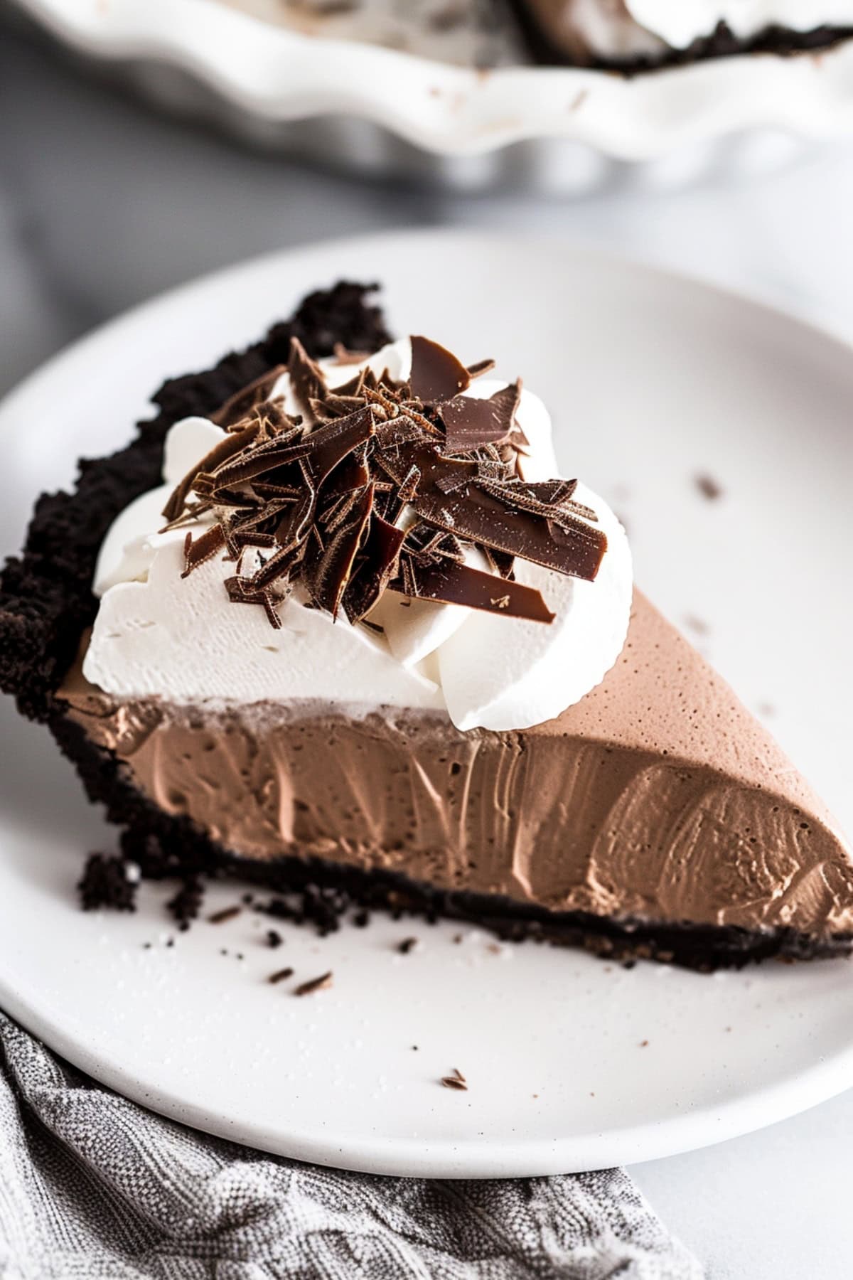 A decadent slice of French silk pie topped with whipped cream and chocolate shavings on a white plate