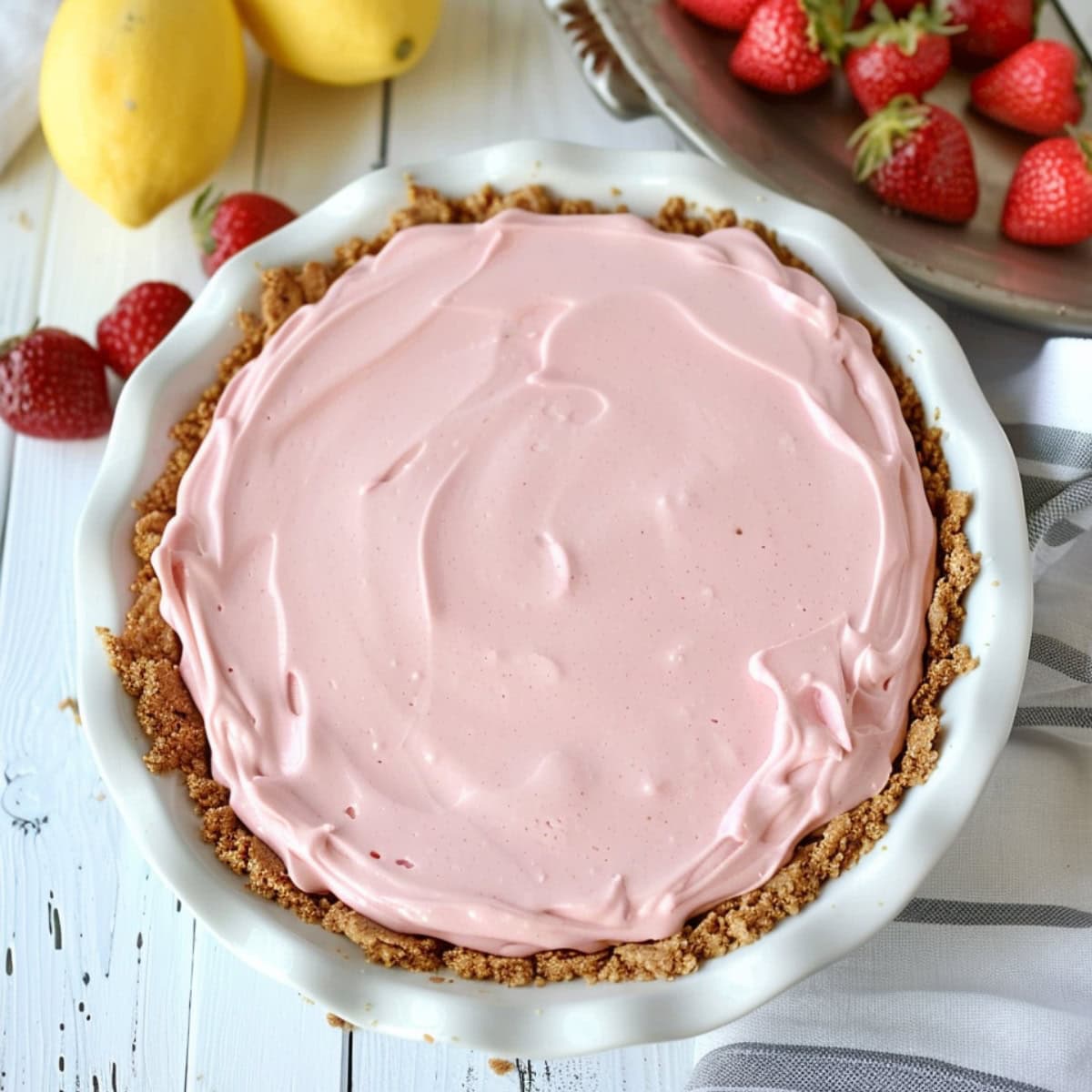 Whole creamy frozen strawberry lemonade pie on a round baking dish on wooden table.