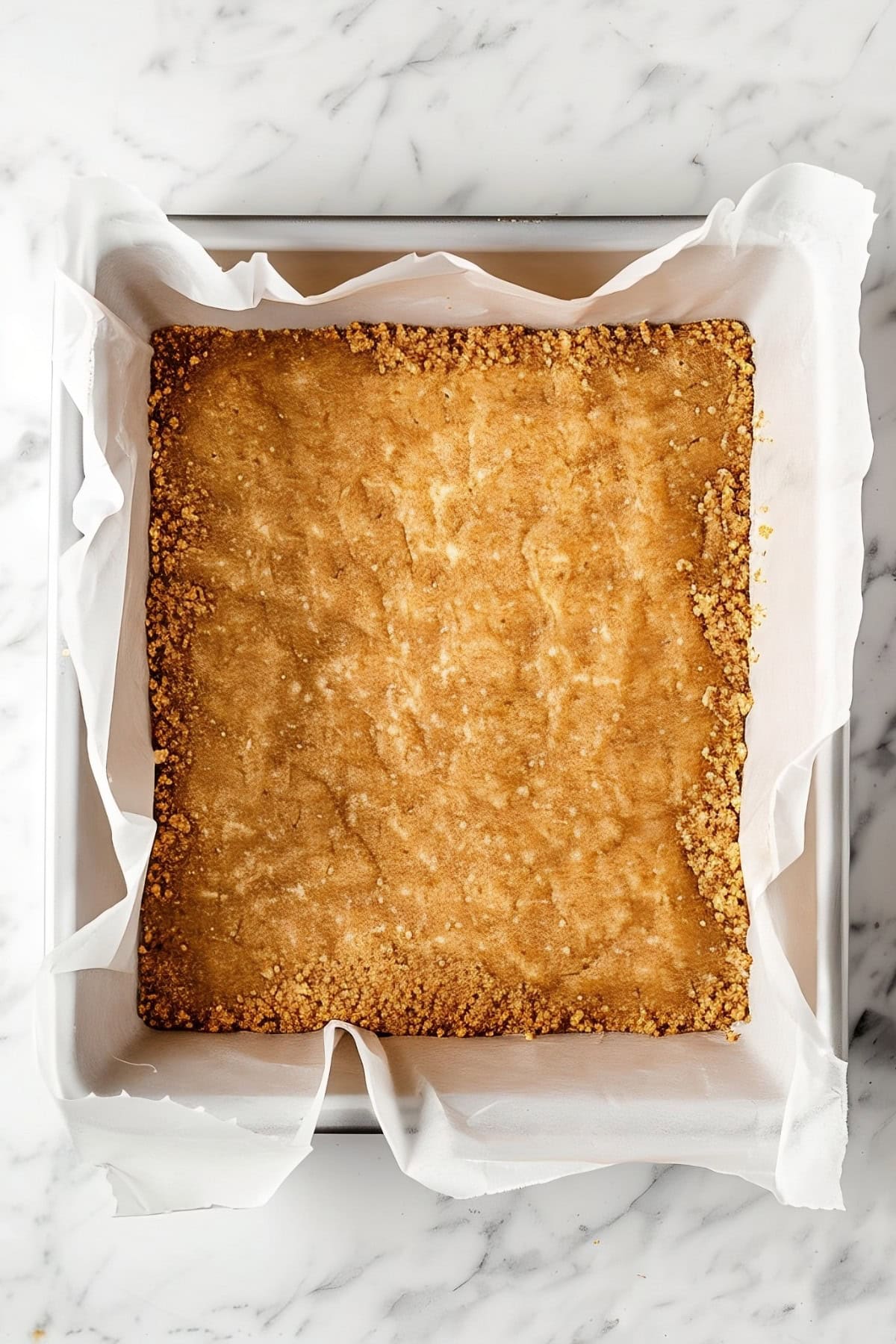 A rectangle baking dish of crushed grahams on a white marble countertop