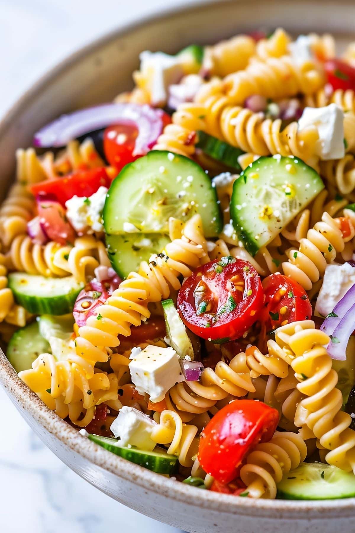 Close Up of Greek Pasta Salad in a Bowl with Fresh Cucumbers Slices, Tomatoes, Red Onion, Feta, and Rotini Pasta with Lemon Juice and Seasonings