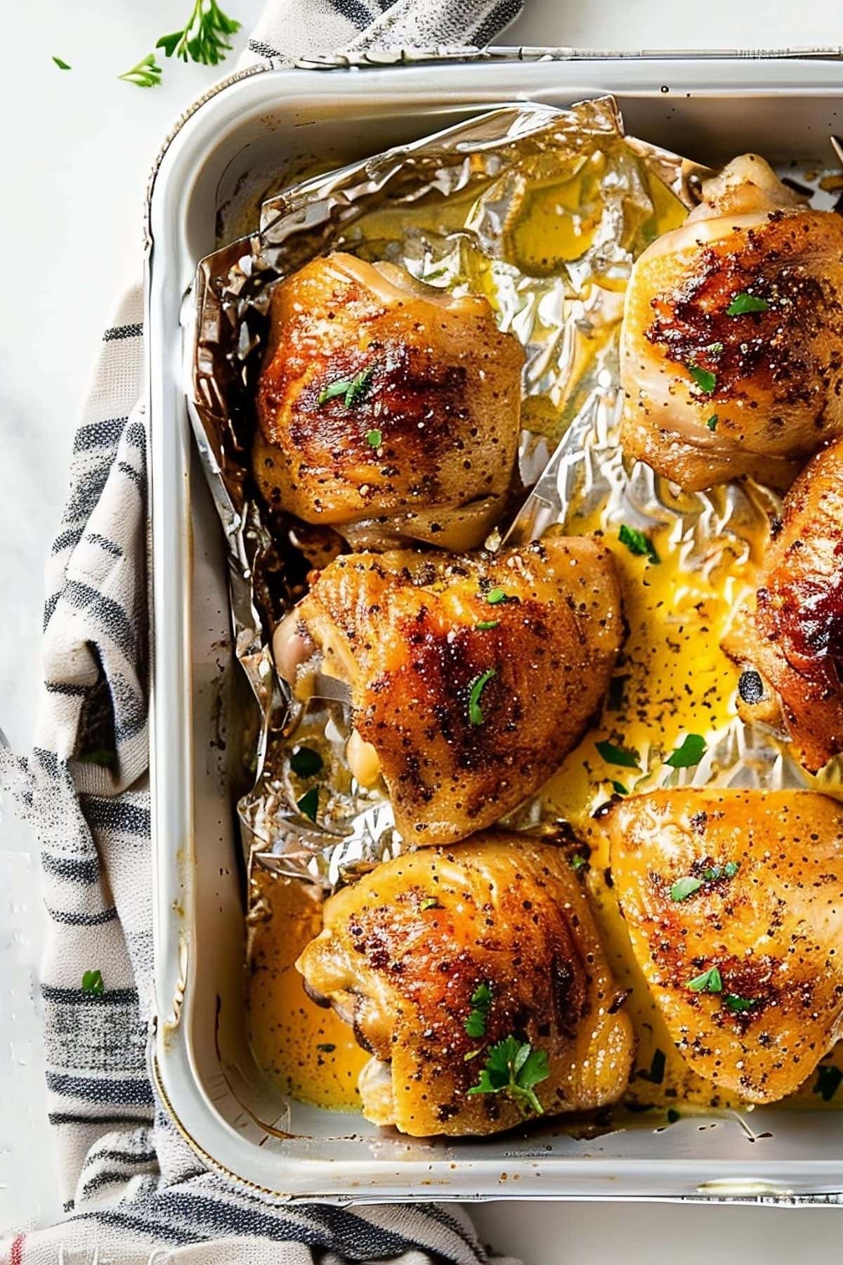 Close Up Crispy Oven-Baked Chicken Thighs in the Baking Tray with a Blue-Striped Kitchen Towel