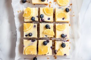 Lemon blueberry cheesecake bars arranged neatly on a white parchment paper.