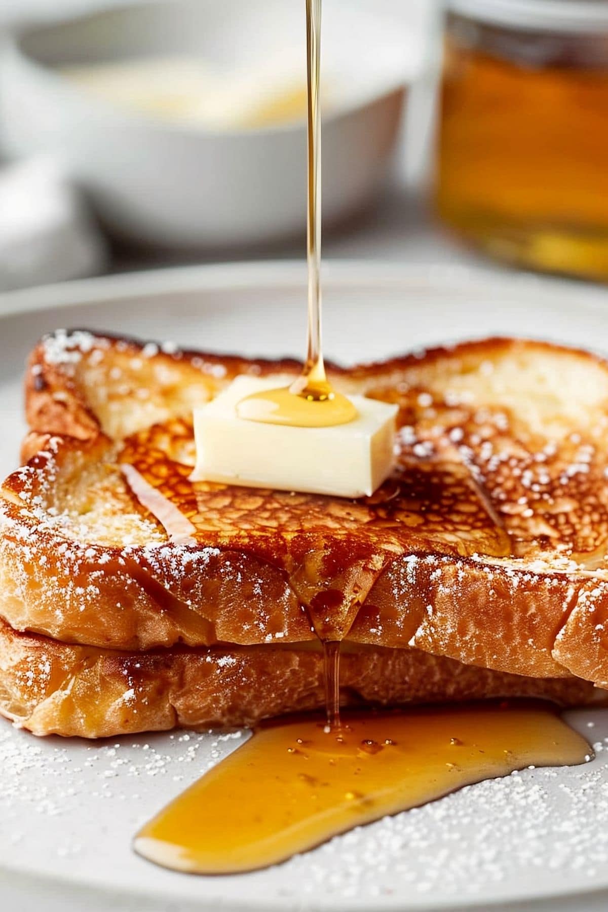 Side View of Pouring Maple Syrup Onto Two Slices of McCormick French Toast with Butter and Powdered Sugar on a White Plate
