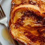 Super Close Up of Caramelized McCormick French Toast with Powdered Sugar and Maple Syrup on a White Plate with a Fork