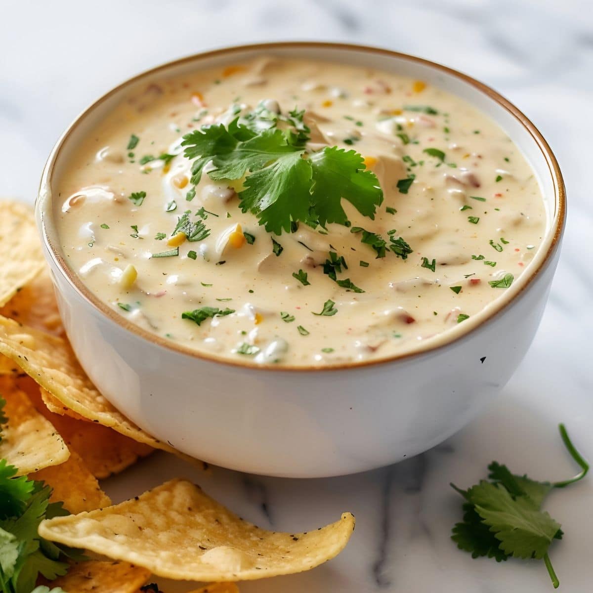 Top Side View of a Bowl of Mexican White Queso Cheese Dip with Cilantro on a White Marble Table with Chips