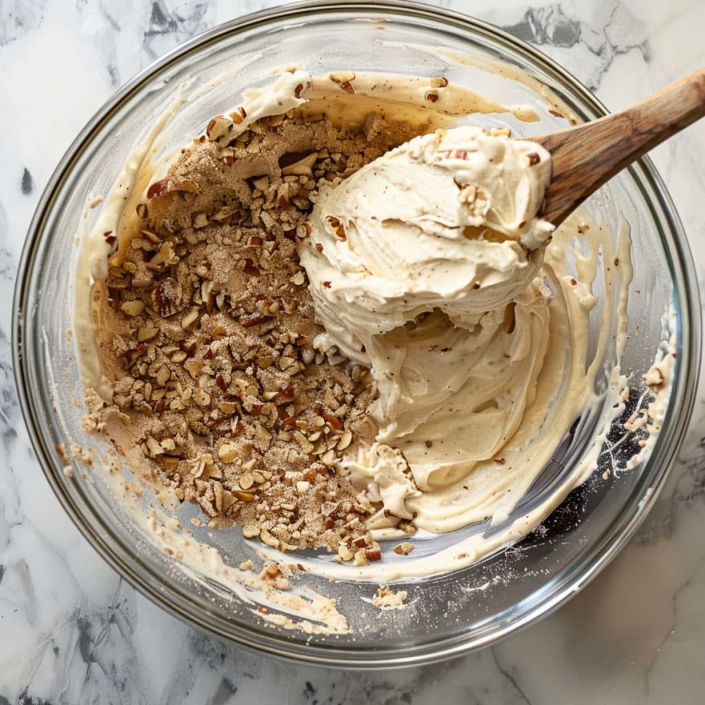 A glass bowl of mixed cream cheese and crushed pecan nuts on a white marble countertop