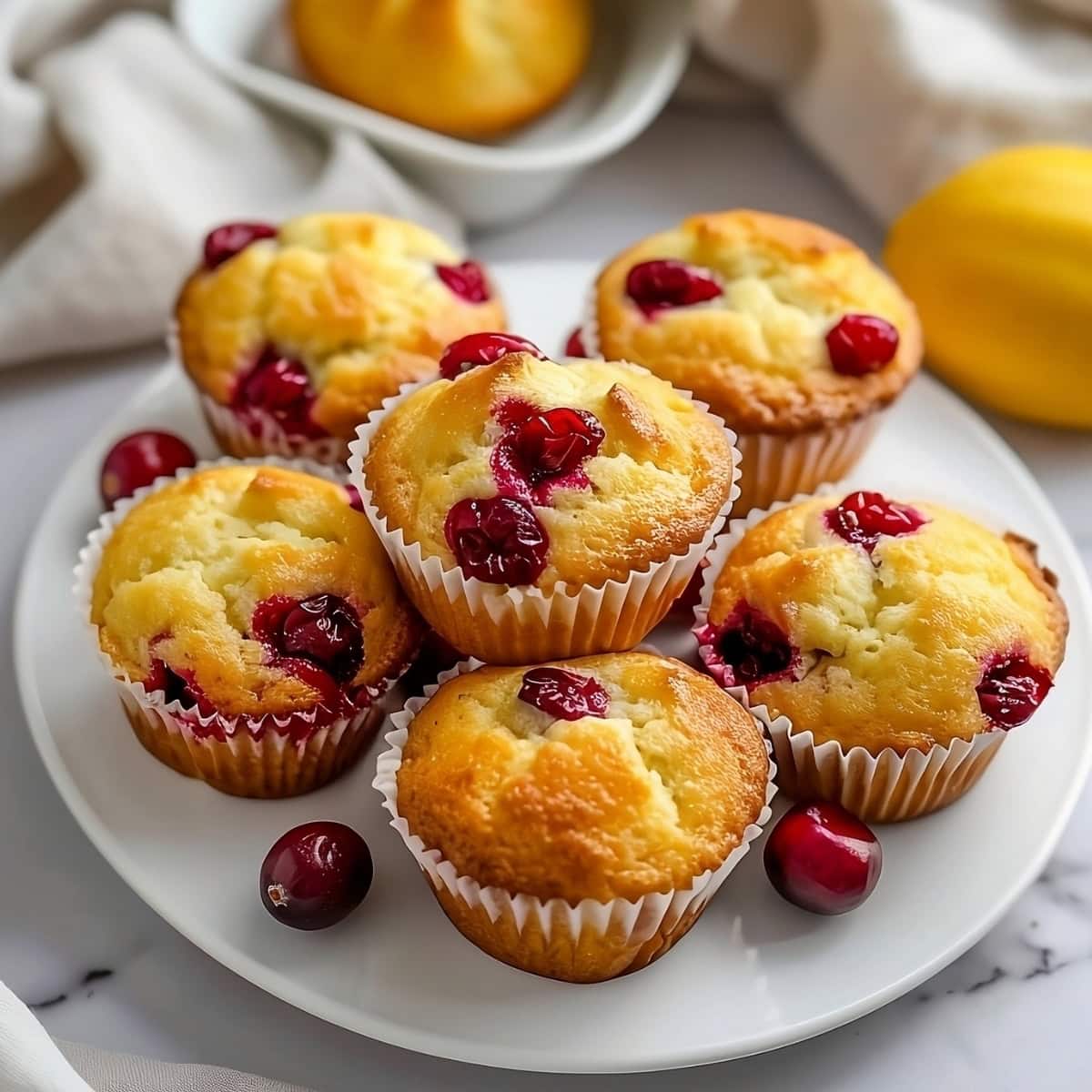 Cranberry lemon muffins arranged in a white plate on a white marble surface.