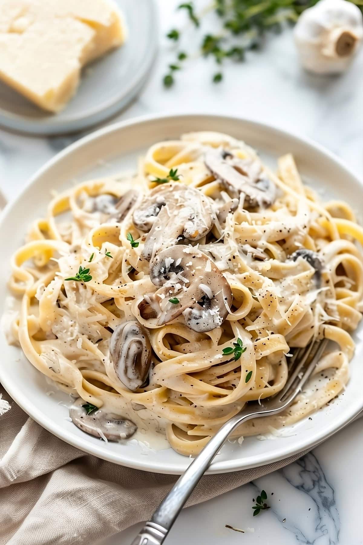 Mushroom pasta in creamy sauce garnished with parmesan cheese served in a white plate.