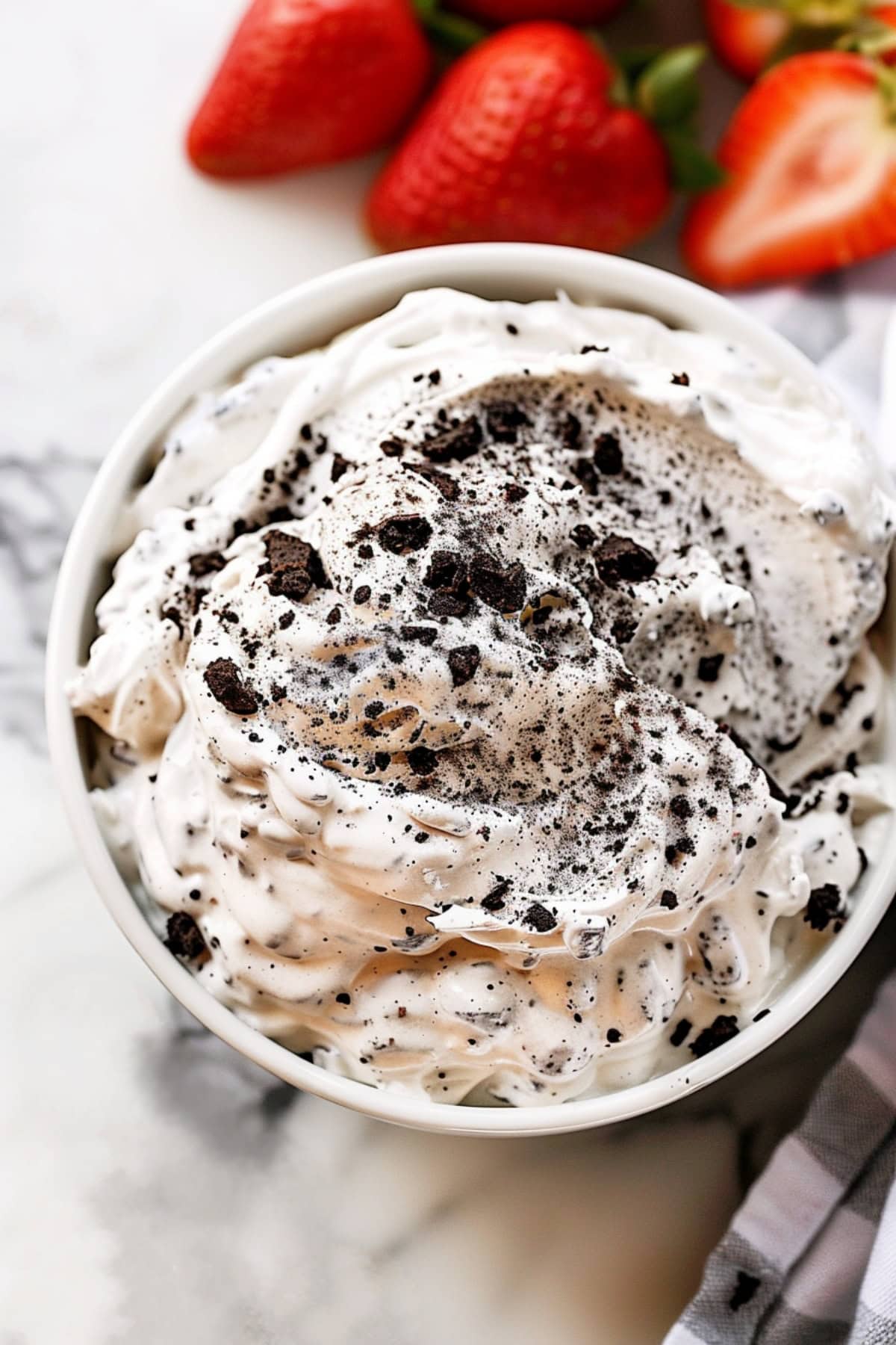 Oreo dip in a bowl paired with fresh strawberries in a white marble countertop