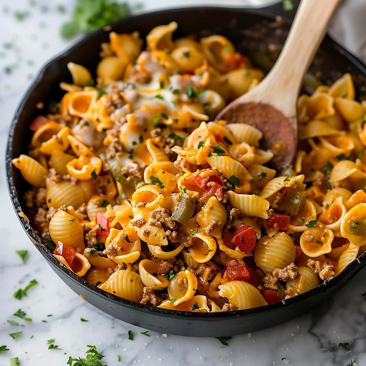 Taco pasta tossed in skillet pan with a wooden ladle.