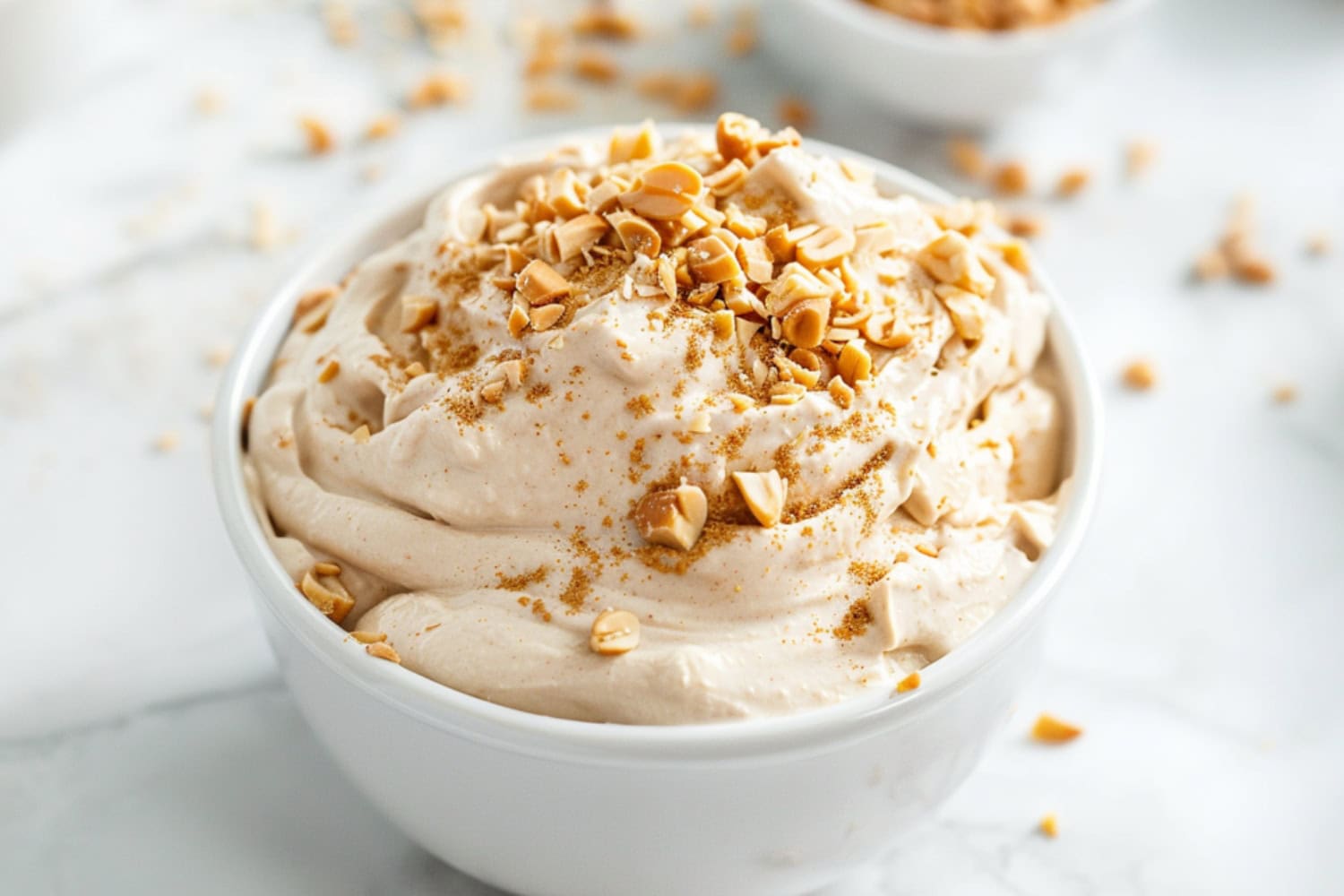 Fluffy and creamy peanut butter dip in a white bowl topped with chopped peanuts.