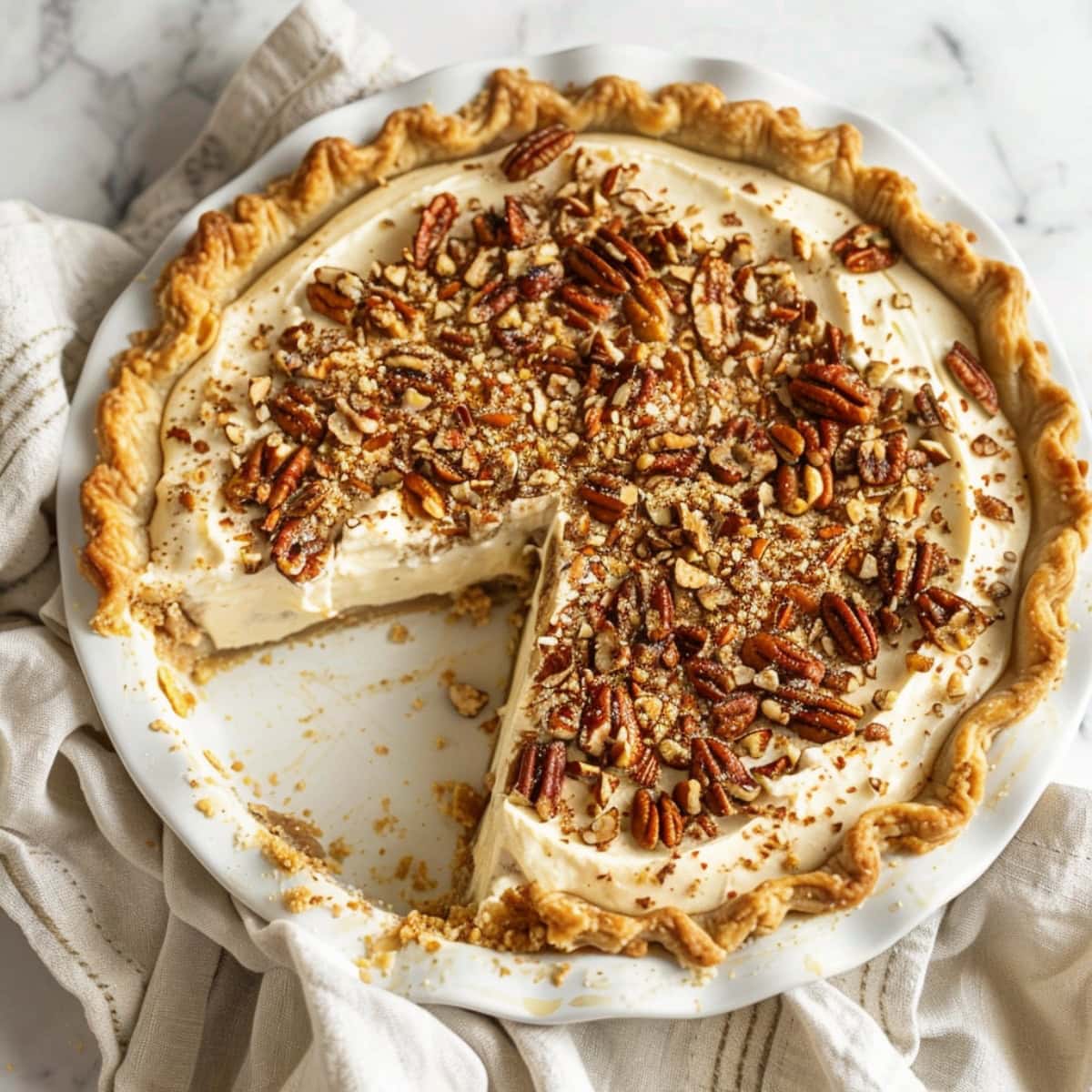 Whole pecan cream pie with a slice removed in a white ceramic pie dish