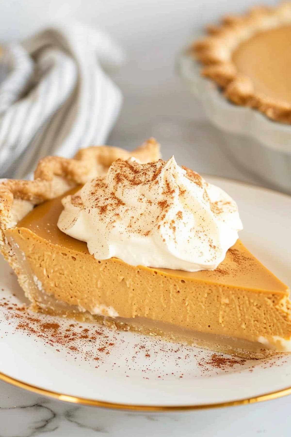 Slice of pumpkin cream pie served on a white plate with whipped cream, dusted with pumpkin spice.