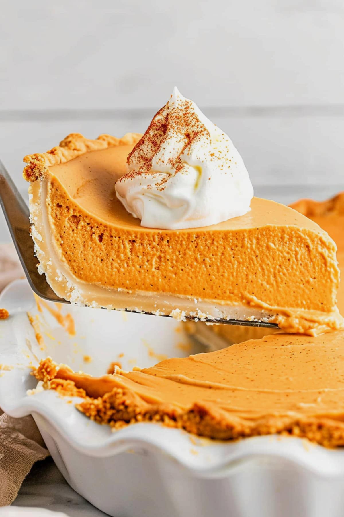 Pie ladle lifting a serving of pumpkin cream pie from the baking dish.