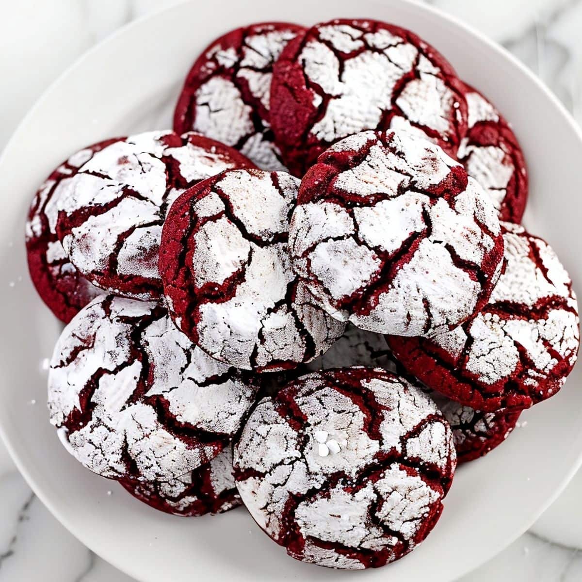 Top View of Pile of Red Velvet Crinkle Cookies with Powdered Sugar on a White Plate