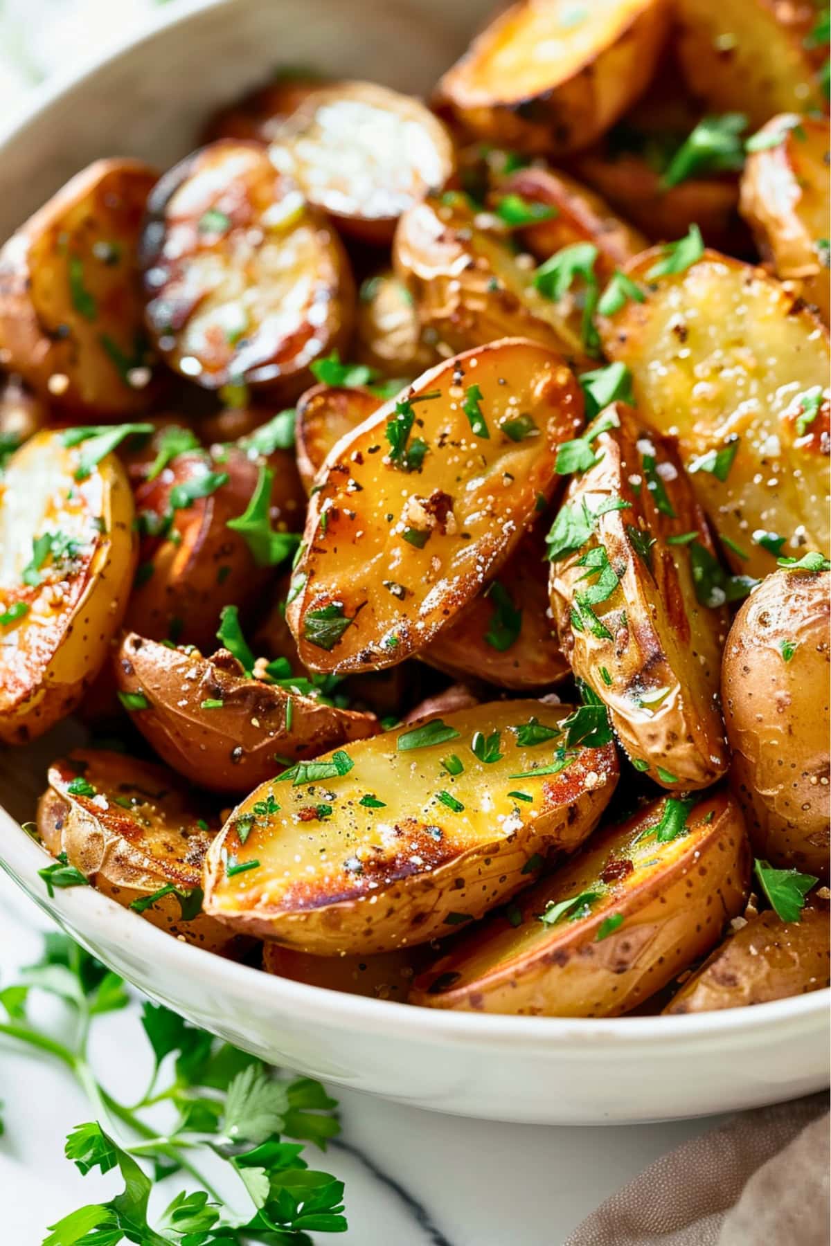 White bowl with roasted fingerling potatoes sliced in half garnished with chopped parsley.