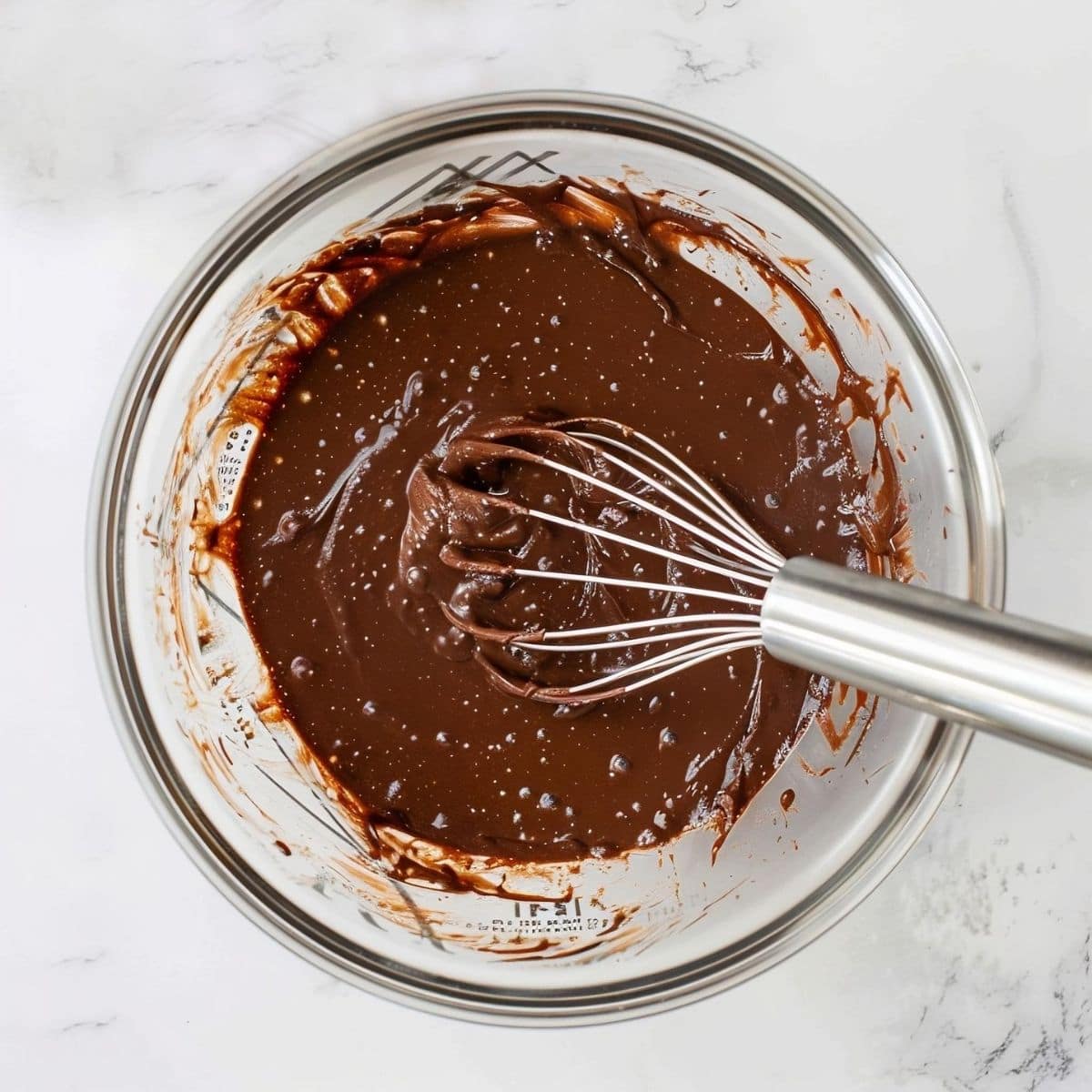 Top View Coca Cola Cake Batter in a Glass Bowl with a Whisk on a White Marble Table