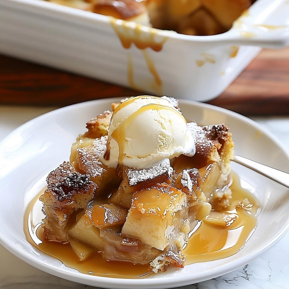 Apple pie pudding slice on a white plate with vanilla ice cream on top.