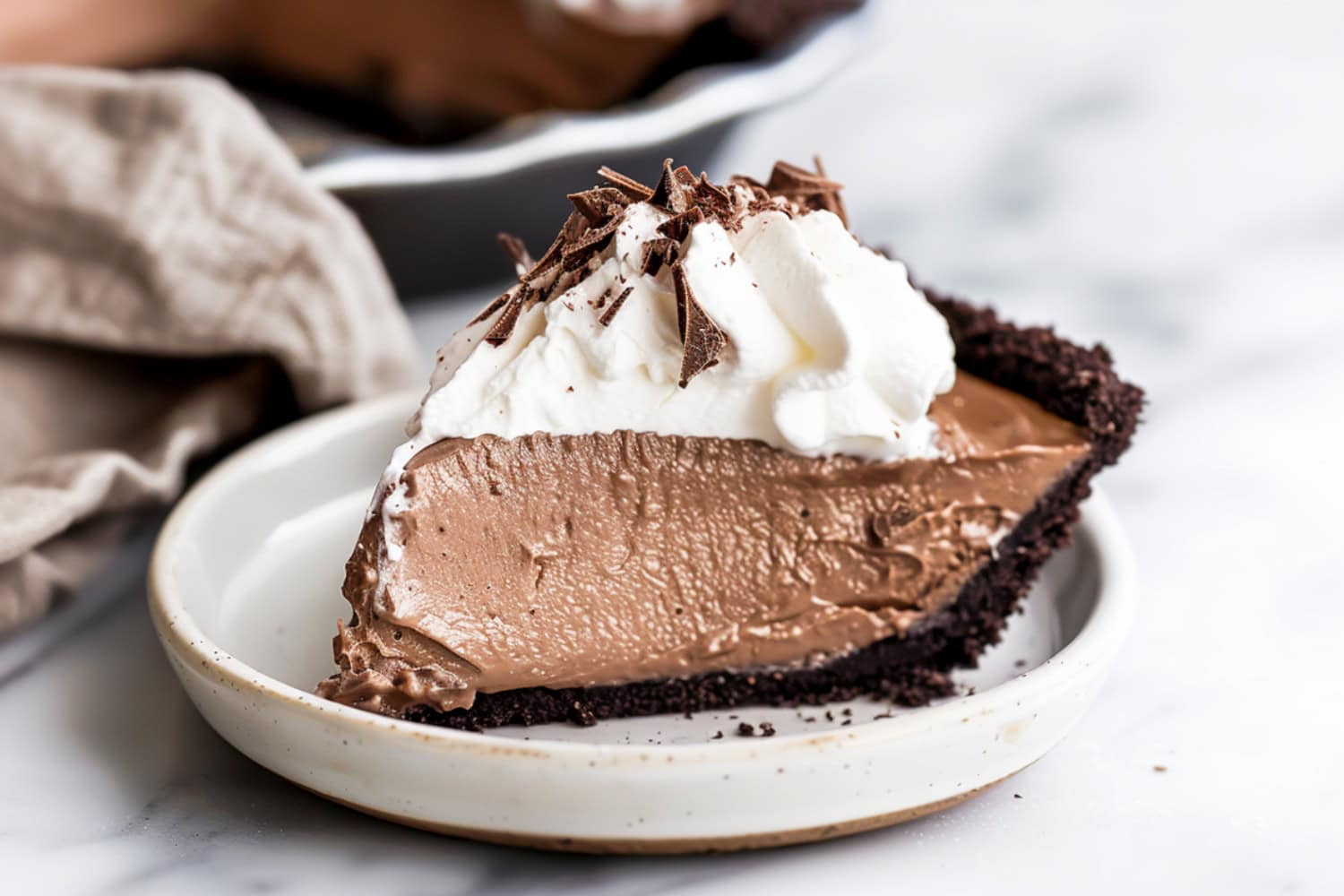 French silk pie served on a dessert plate with a dollop of whipped cream and chocolate shavings