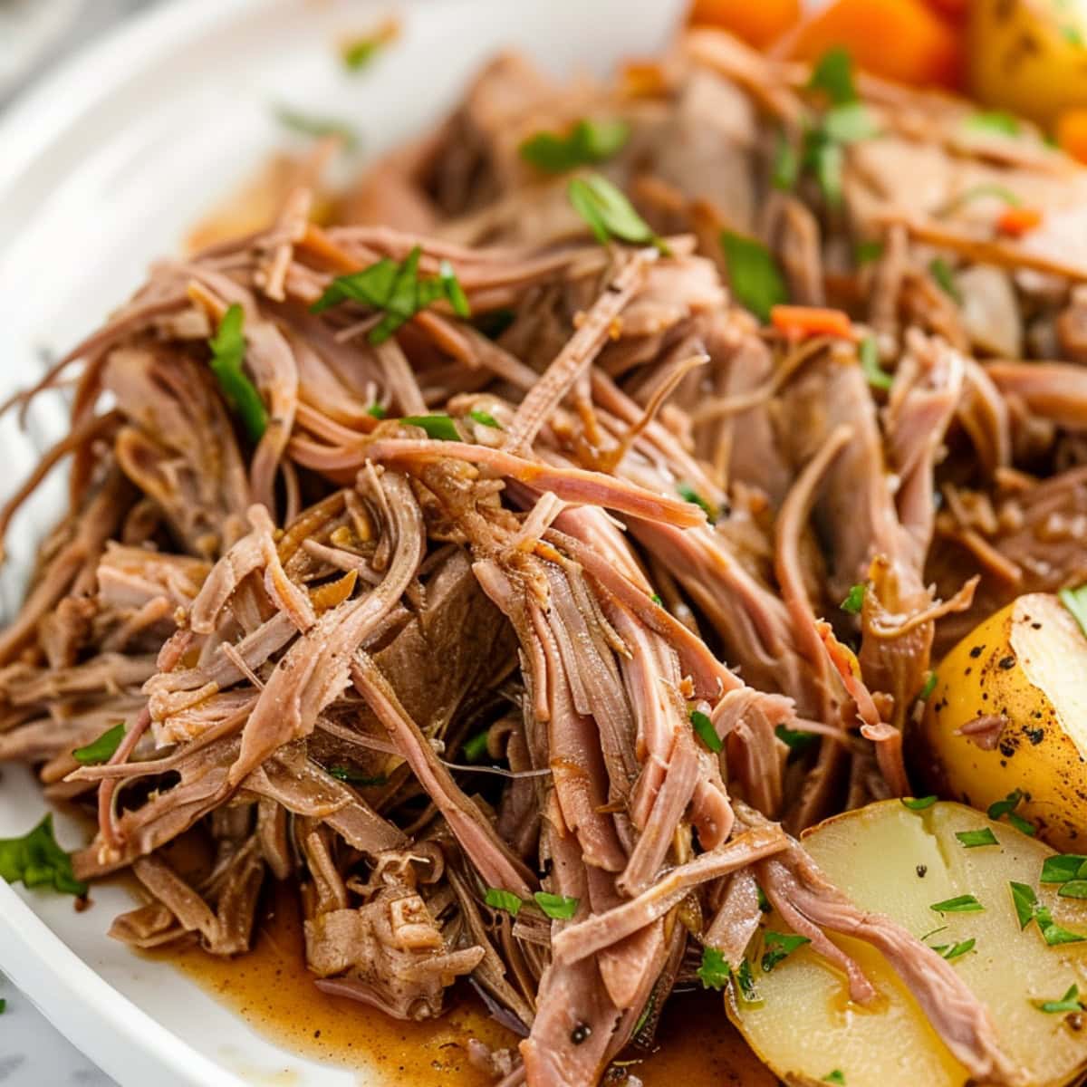 Serving of shredded slow cooker pork roast in a plate with potatoes and carrots.