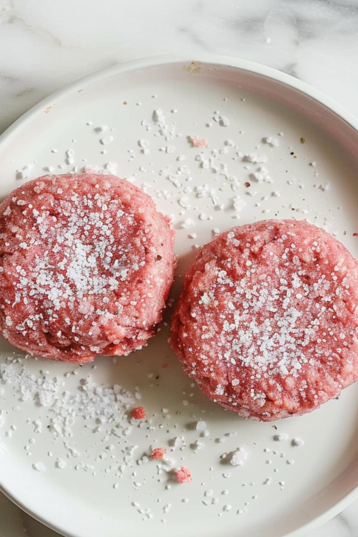 Pressed raw patties sprinkled with salt on a white plate.