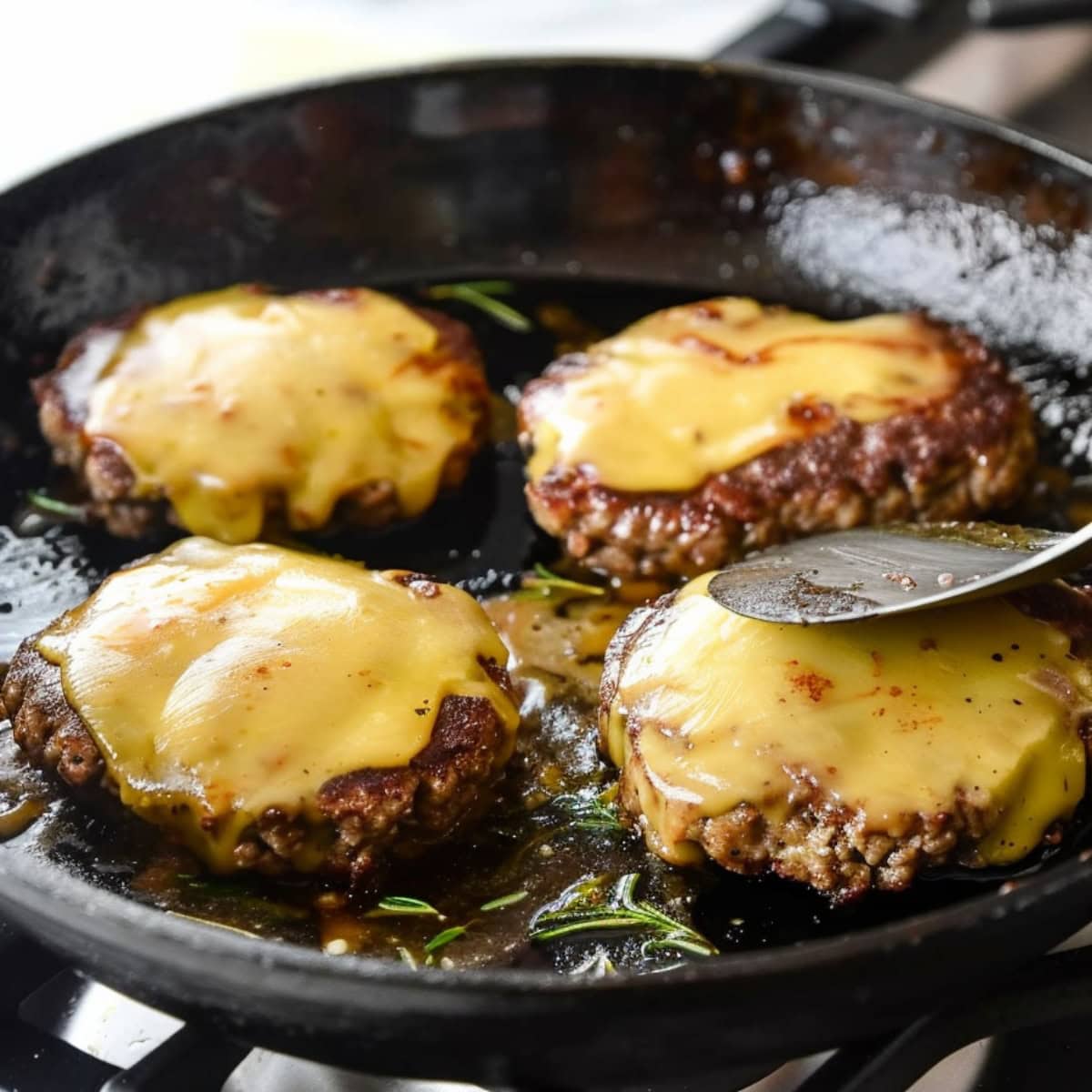 Patties topped with cheese on a skillet.