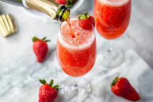 Sparkling wine pouring to a glass with strawberry puree garnished with fresh strawberries.