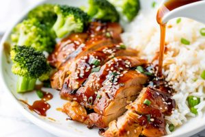 Teriyaki sauce poured to sliced chicken thigh served with broccoli and white rice.