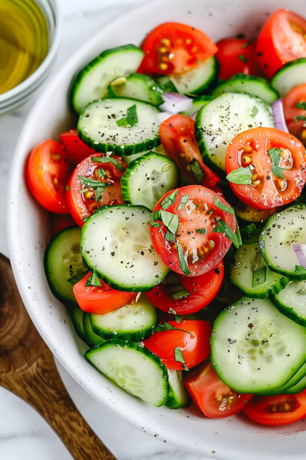 Vibrant tomato and cucumber salad with red onions, garnished with fresh basil and a drizzle of olive oil.