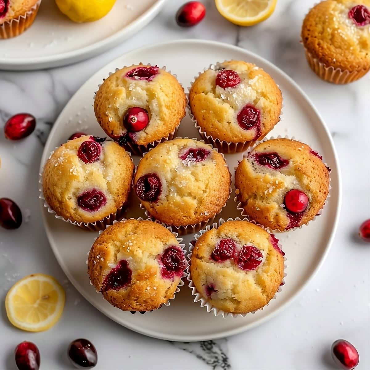 Top view of bunch of cranberry lemon muffins in a white plate.