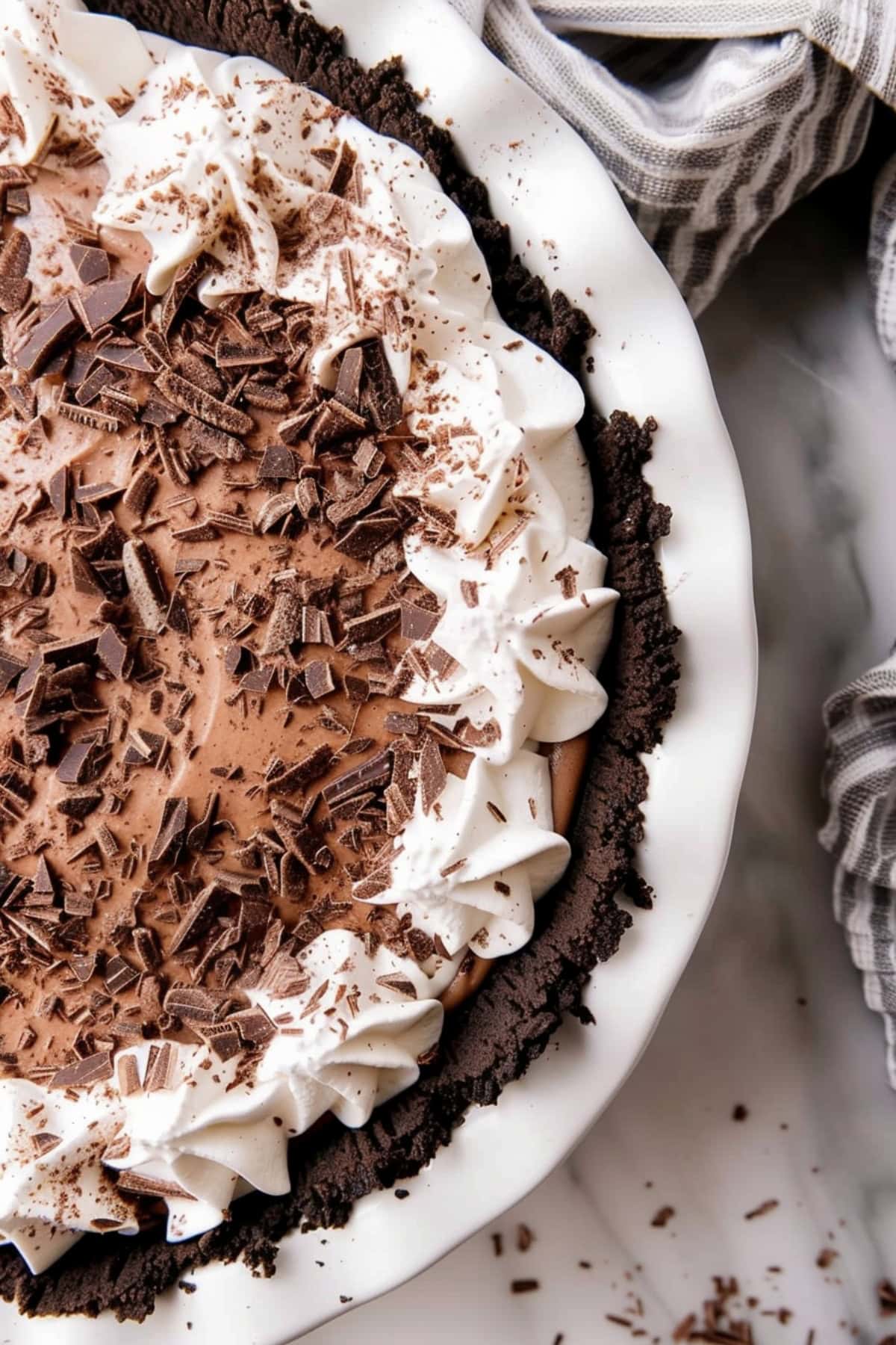 Whole chocolate French silk pie topped with whipped cream and chocolate shavings on white marble countertop