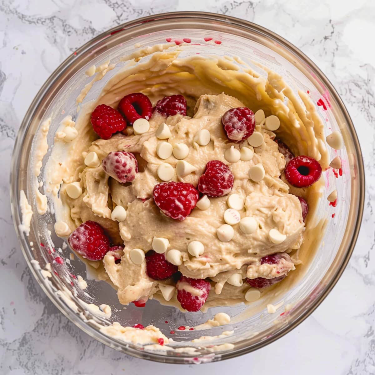 White chocolate chip and raspberry muffin batter in a glass bowl, top down view