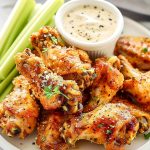 Close Up of a Pile of Crispy, Seasoned Wingstop Garlic Parmesan Wings with Celery and Ranch Dip on a White Plate