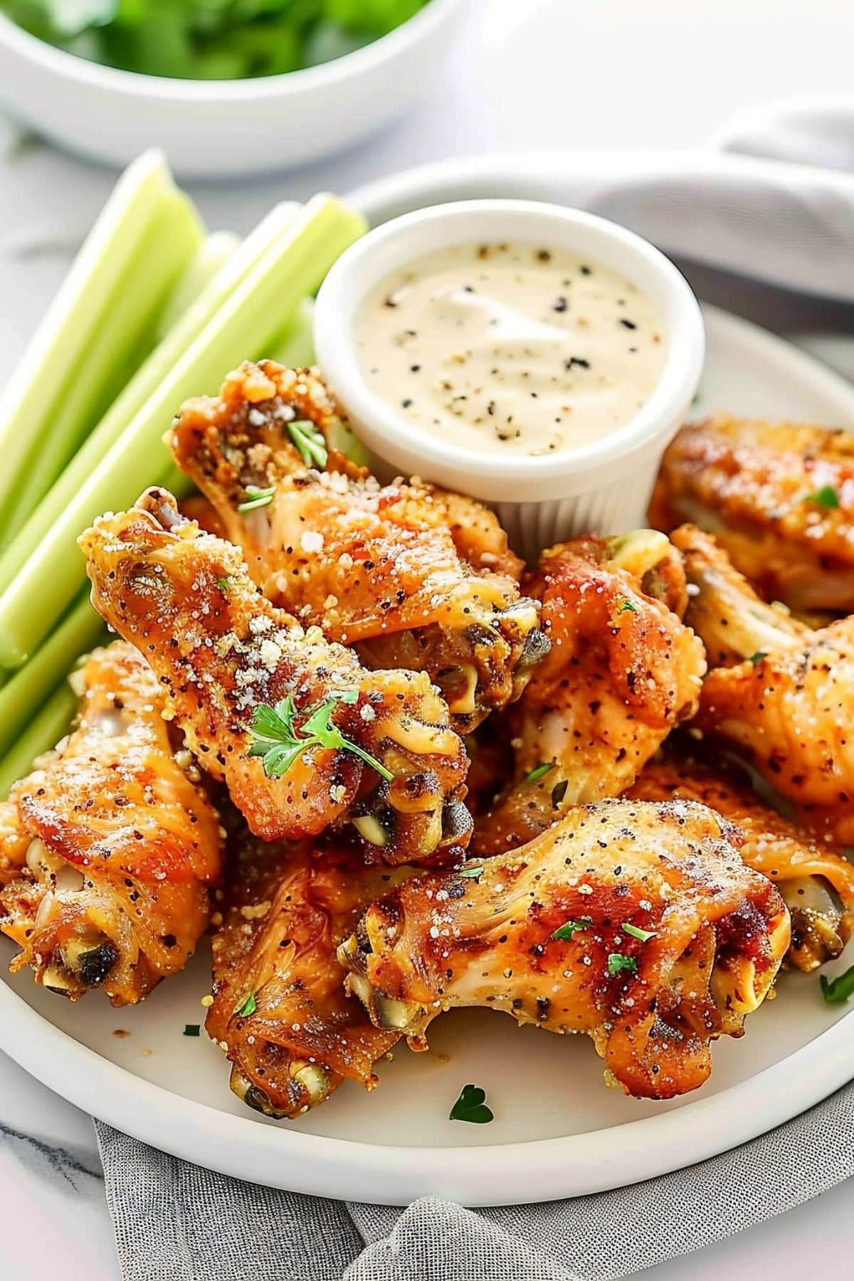 Close Up of a Pile of Crispy, Seasoned Wingstop Garlic Parmesan Wings with Celery and Ranch Dip on a White Plate