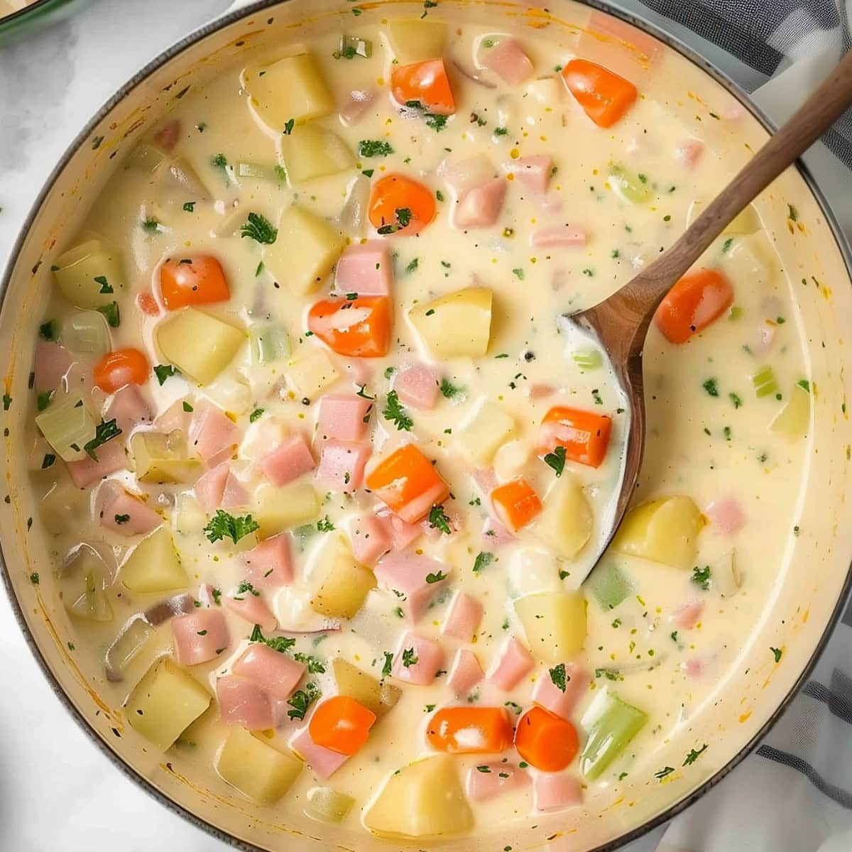 Top View of Ham and Bean Soup with Chunks of Ham, Potatoes, Carrots, Celery, Onions, and Seasonings in a Dutch Oven with a Wooden Spoon