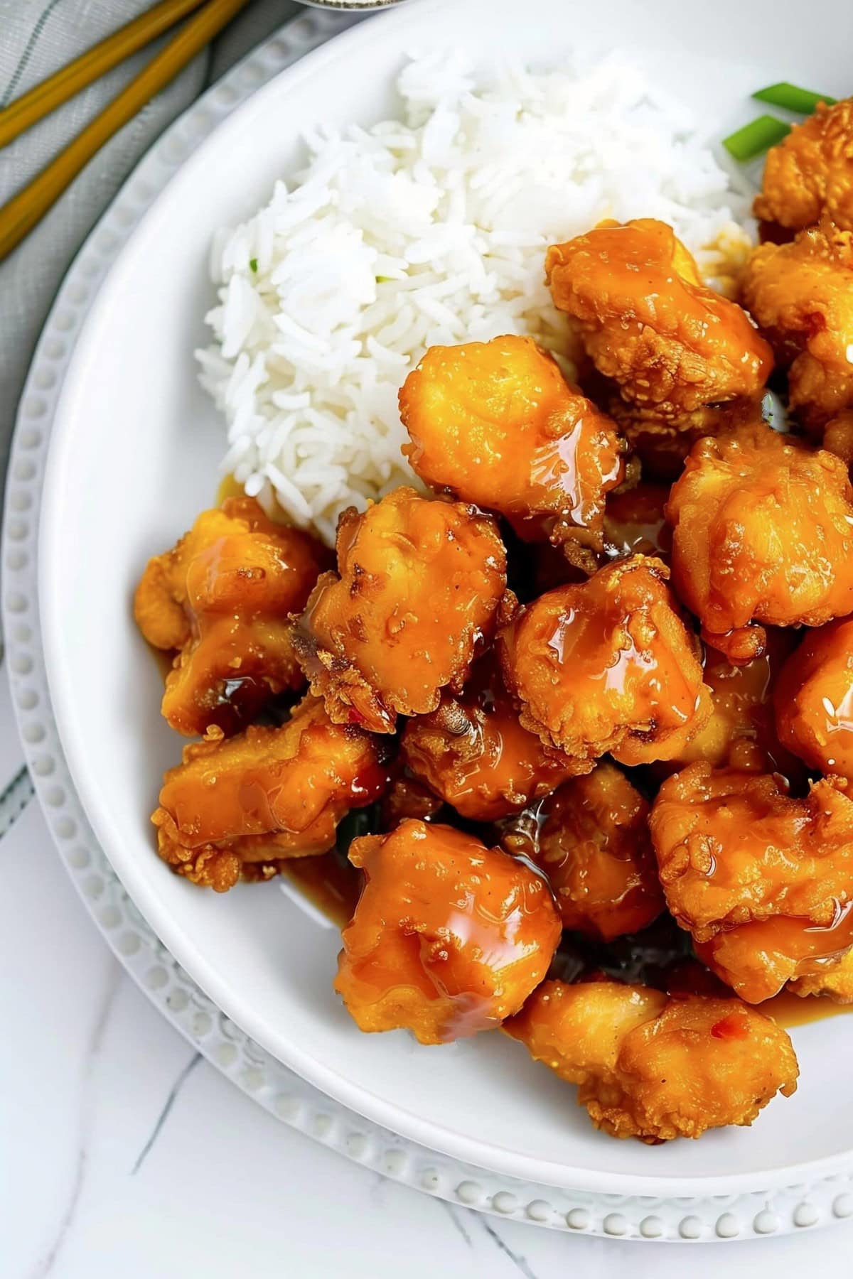 Sweet and Sour Chicken Balls on a Plate with Rice, Scallions, and Chopsticks to the Side