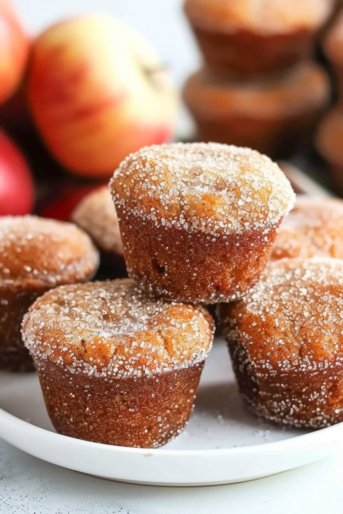 Bunch of apple cider donut muffins coated in cinnamon sugar arranged in a white plate.