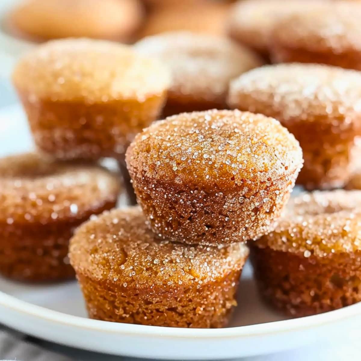 Bunch of apple cider donut muffins arranged on a white plate.