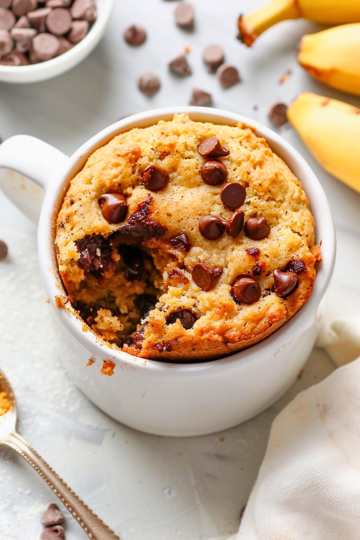 Scoop missing banana cake in a white mug topped with chocolate chips.