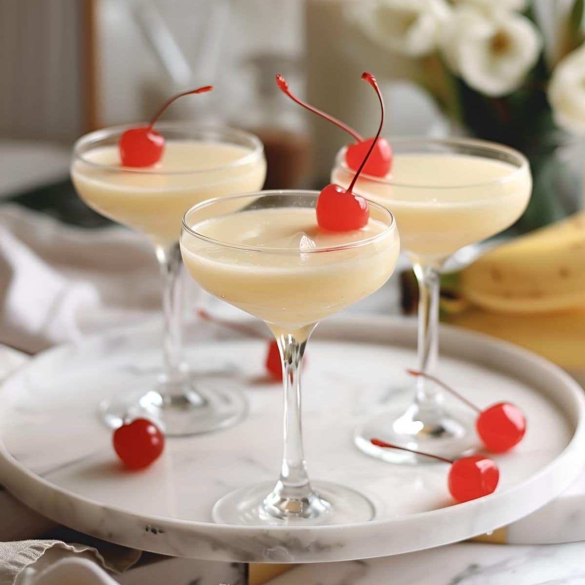 Three Banana Daiquiris in Glasses with Maraschino Cherries on a White marble Serving Tray