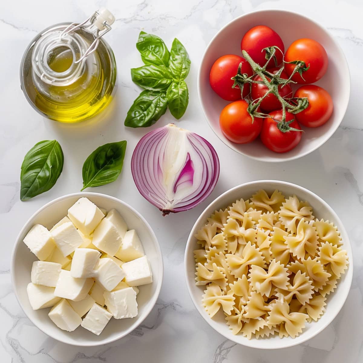 Cherry tomatoes, cubed mozzarella cheese, onion, bowties pasta and olive oil on a white marble table. 