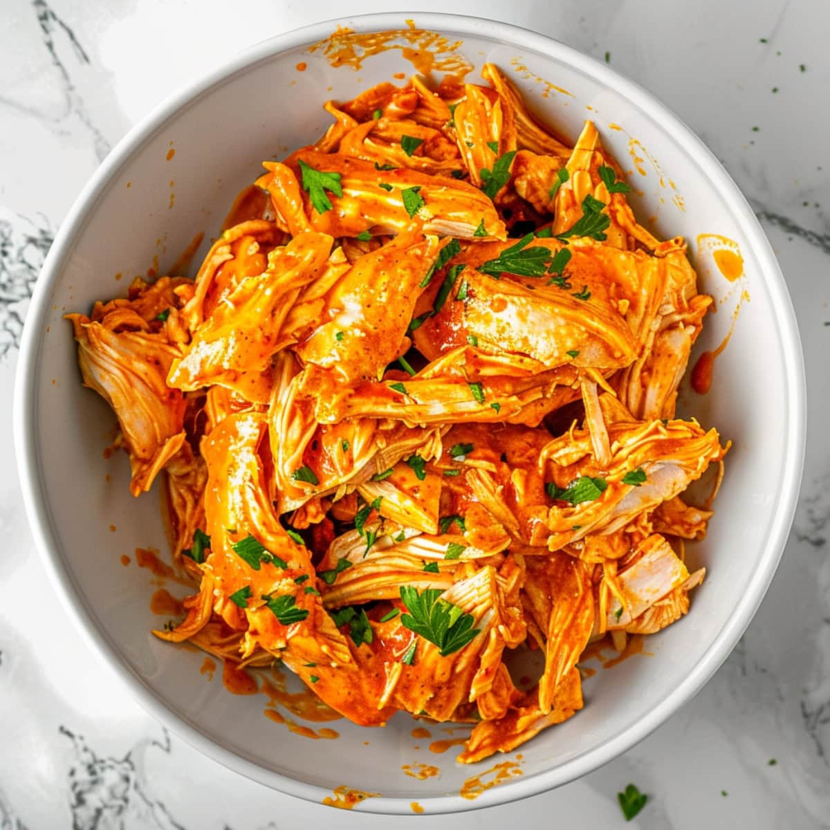 Bowl of shredded chicken covered in buffalo sauce.