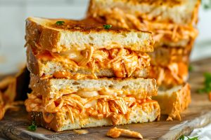 Grilled cheese sandwich with buffalo chicken filling on a wooden cutting board.