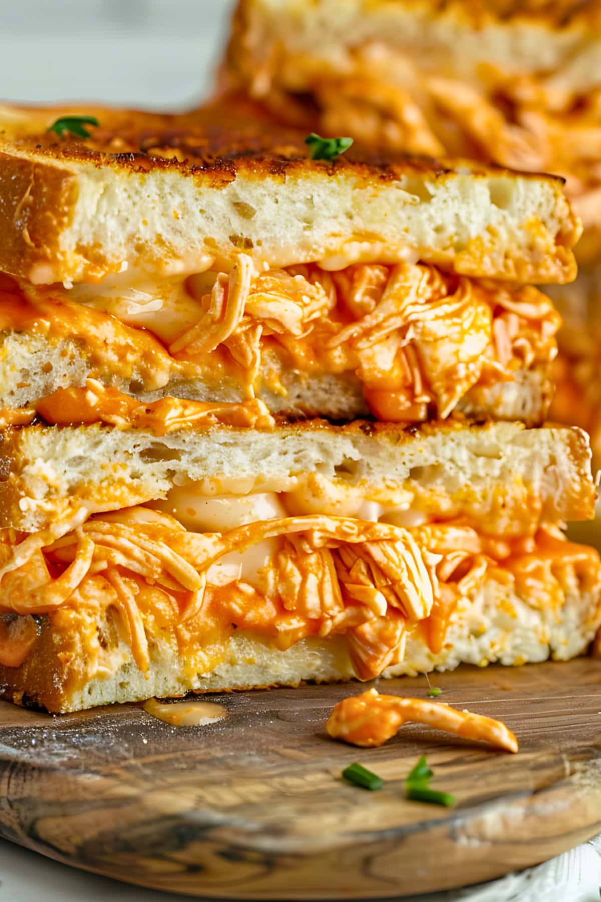 Grilled sandwich with cheesy buffalo chicken filling stacked on a chopping board.