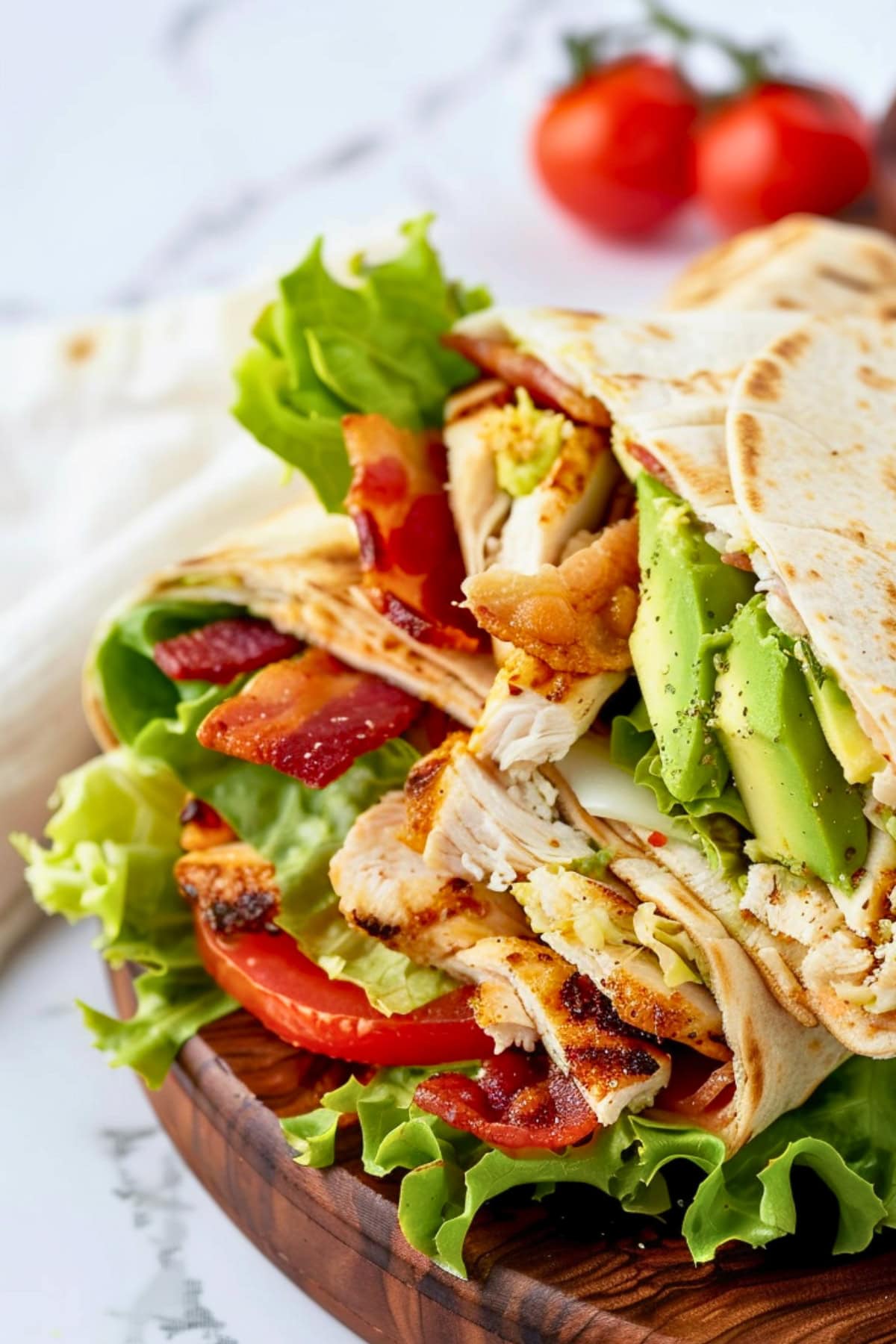 Chicken club wrap stack on each other made with thinly sliced chicken, crisp lettuce, ripe avocado, juicy tomatoes, and crispy bacon in a soft tortilla wrap.