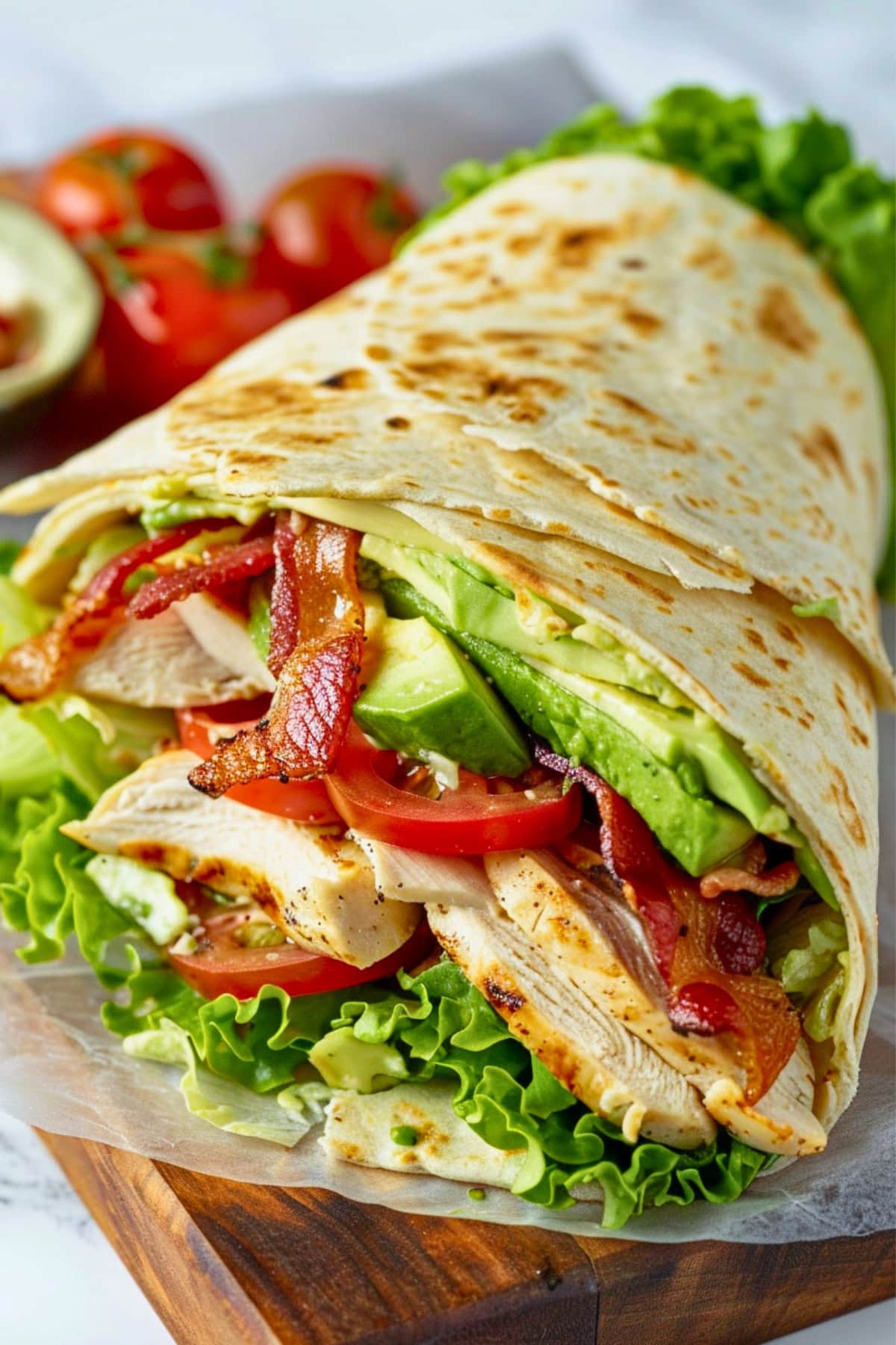 Tortilla wrap made with thinly sliced chicken, crisp lettuce, ripe avocado, juicy tomatoes, and crispy bacon in a soft tortilla wrap.